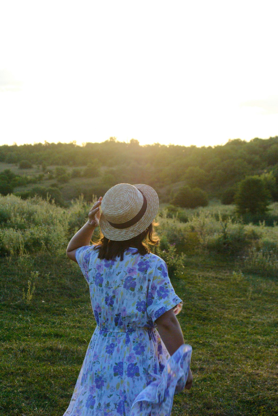 woman in blue and white floral dress wearing brown straw hat standing on green grass field