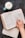A hand is shown resting on an open Bible, specifically on a page that includes the book of 2 Corinthians. Next to the Bible, there is a light blue mug filled with frothy coffee on a dark surface, and an open notebook is mostly out of the frame beneath the Bible.