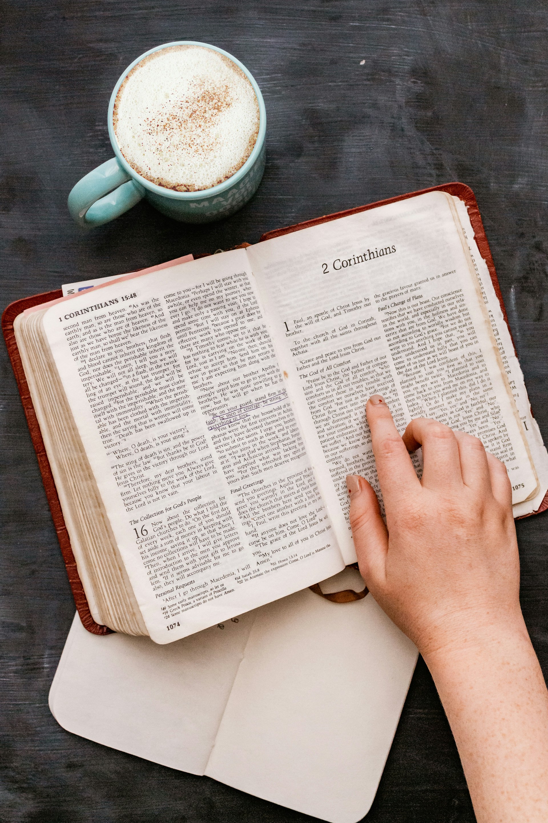 Close-up of a hand holding a Bible next to a coffee cup, with a 'Grace Wins' hoodie visible in the background.