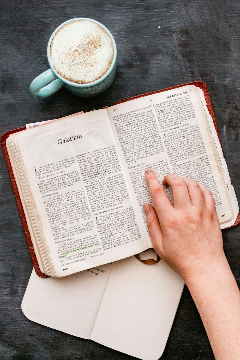 person holding book page near white ceramic mug