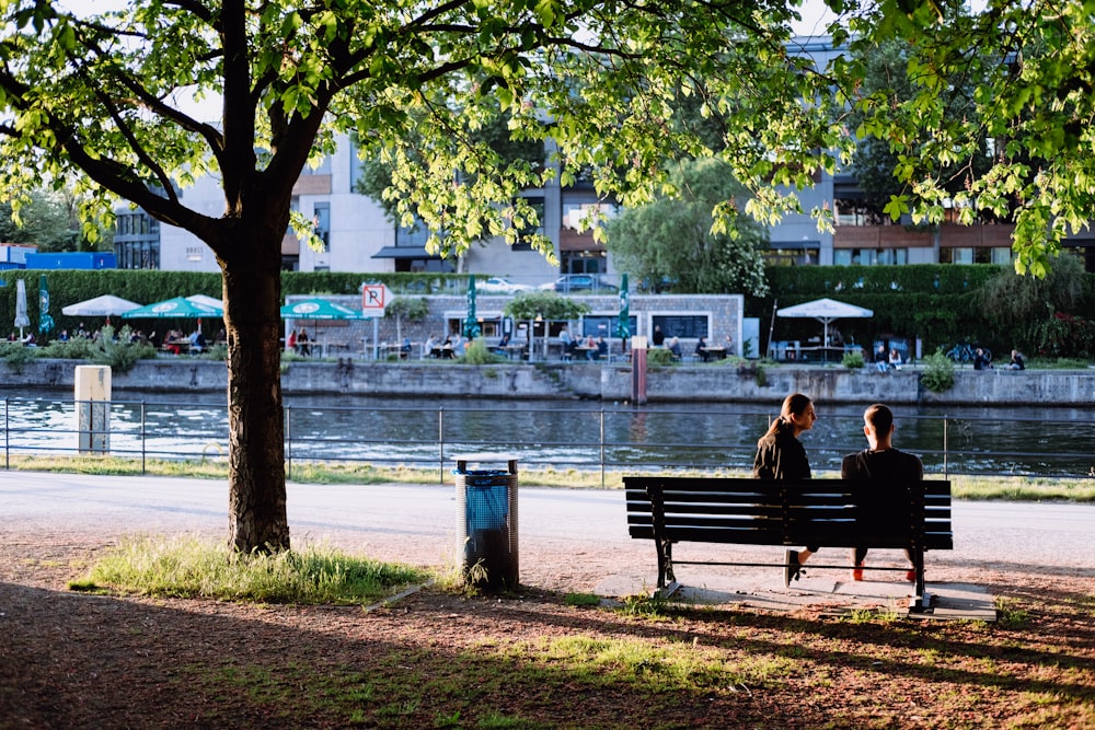man and woman sitting on bench near body of water during daytime