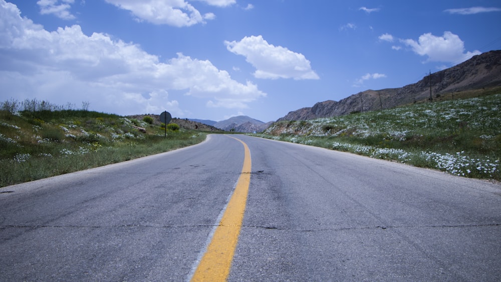 gray concrete road near green grass field under blue sky and white clouds during daytime