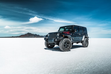 black jeep wrangler on snow covered field under blue sky during daytime