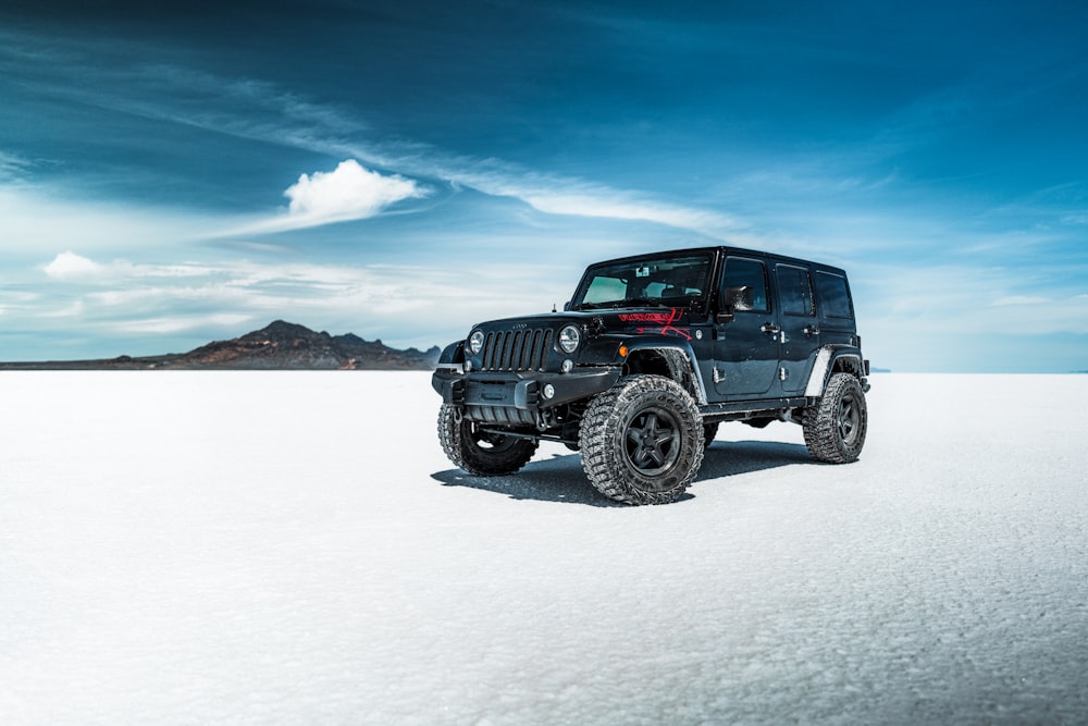 black jeep wrangler on snow covered field under blue sky during daytime