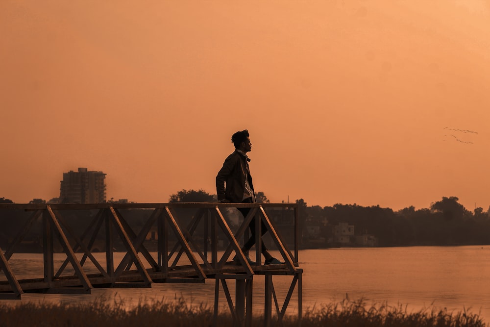 silhouette of man standing on wooden dock during sunset