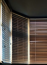 Vertical blinds partially open, allowing light to filter through, creating a pattern of light and shadow on the wooden slats. A mix of warm and cool tones is visible, with contrasting shades on each side influenced by the angle of the light.