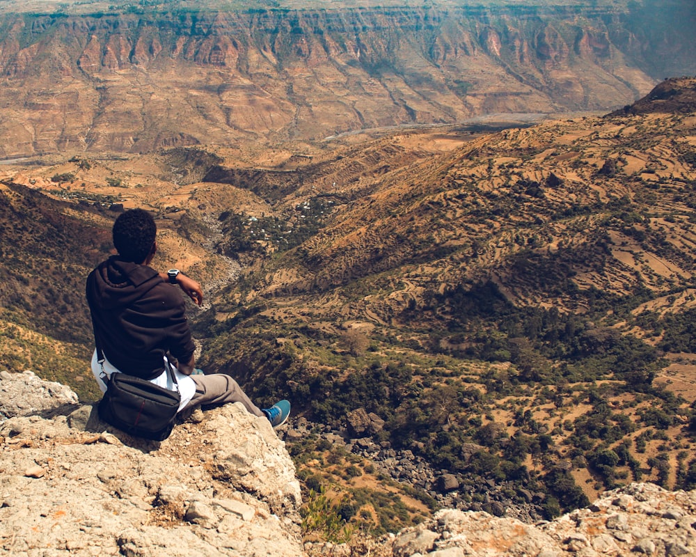 man in black hoodie sitting on rock formation looking at the grand canyon