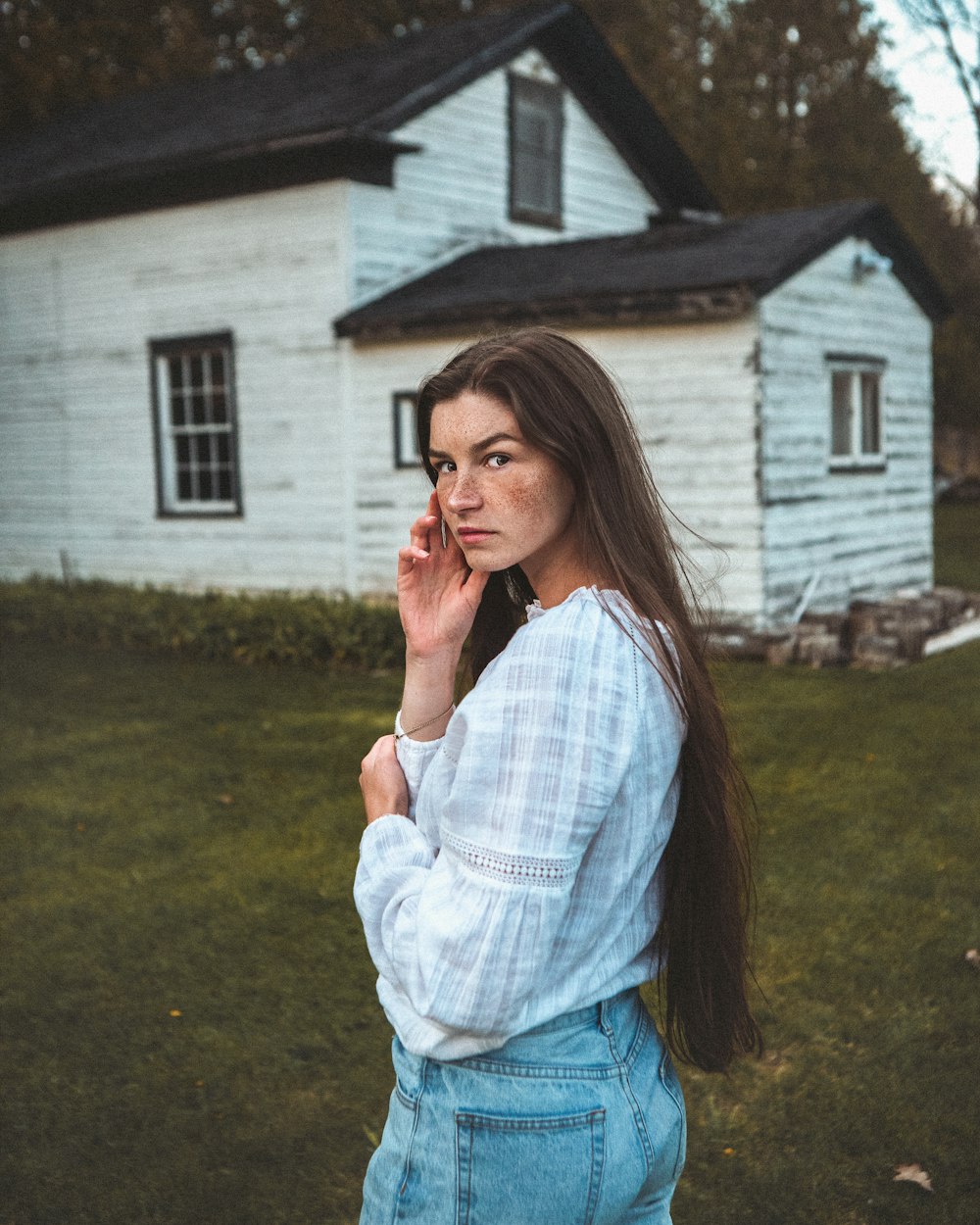 woman in white and blue plaid dress shirt and blue denim jeans standing near white house