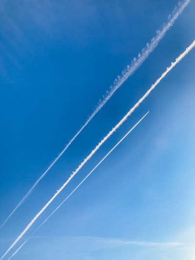 The image highlights a clear blue sky featuring three distinct contrails left by aircraft. The contrails run diagonally across the image, varying in thickness and intensity.