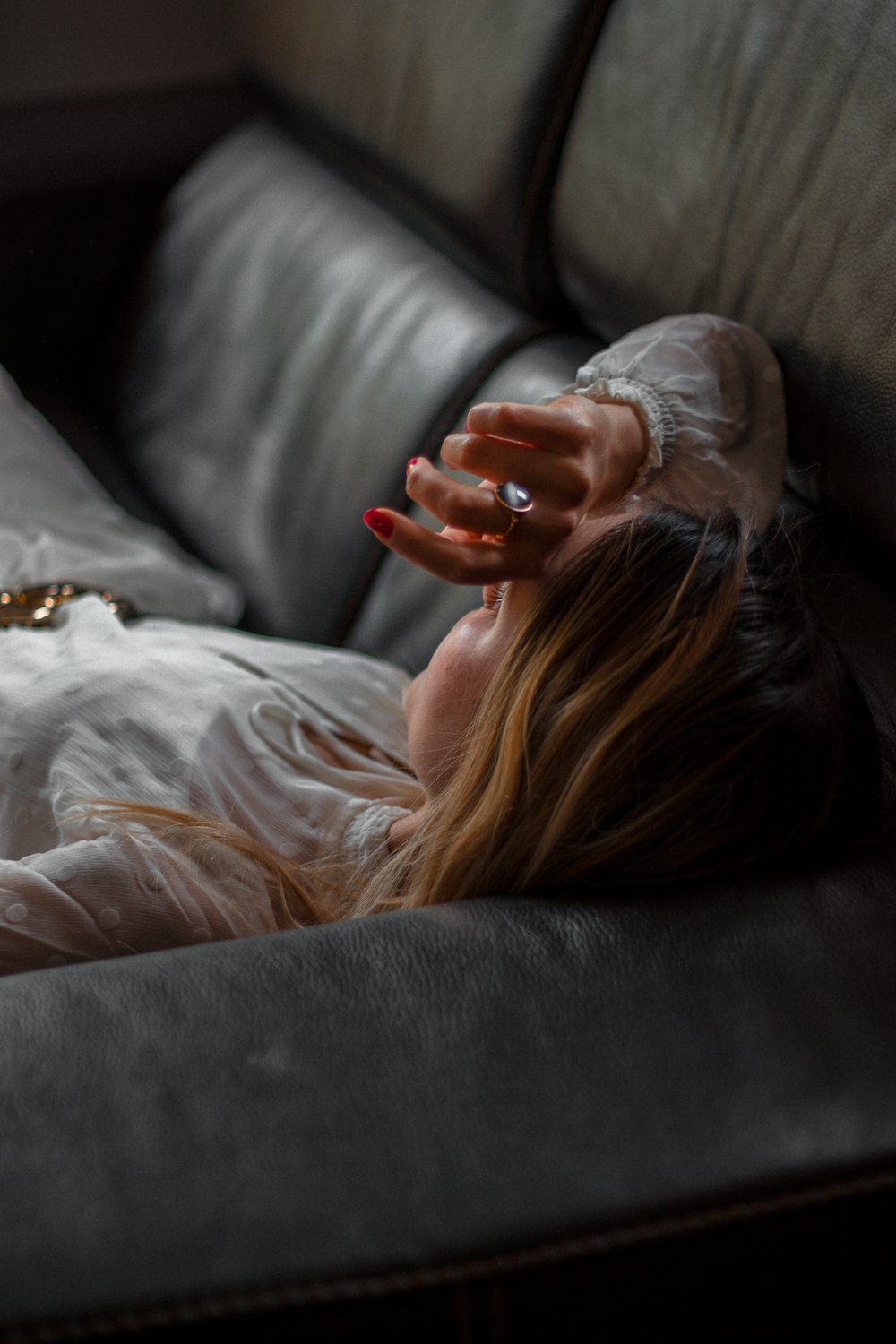 femme en chemise blanche à manches longues allongée sur un canapé noir