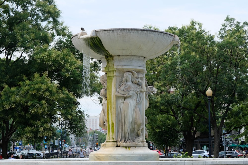 white concrete fountain near green trees during daytime