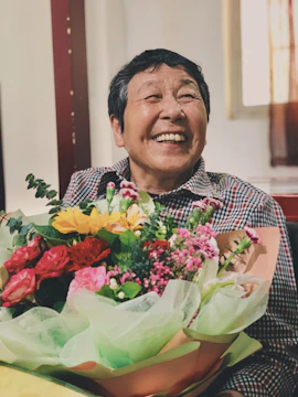 A smiling caregiver handing a flower to an elderly woman at home.