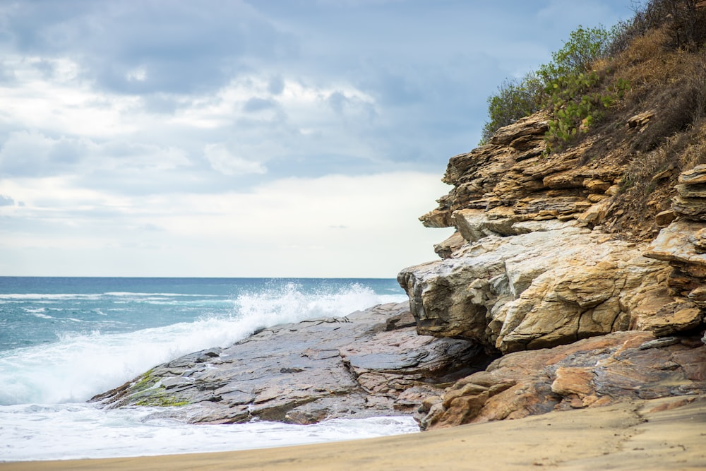 brown rocky shore near body of water under white clouds during daytime