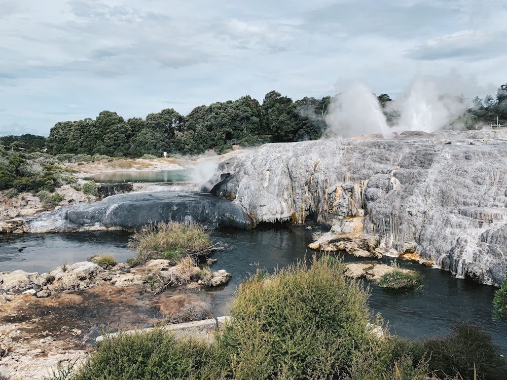 white and brown rock formation near green trees and body of water during daytime