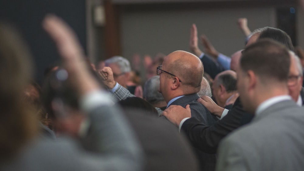 man in black suit jacket raising his right hand