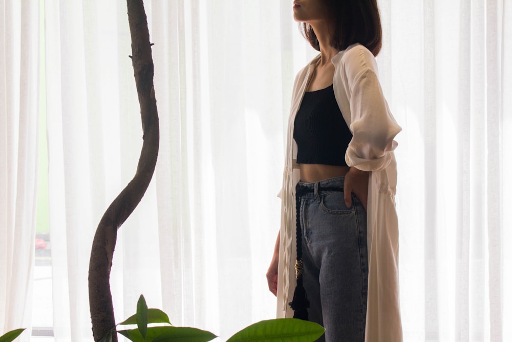 woman in black tank top and blue denim jeans standing beside white curtain