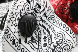 Protective masks featuring intricate black and white paisley patterns alongside a red mask with similar designs. Both masks have a visible black filter attached to them.