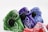 A collection of cloth masks featuring vibrant paisley patterns in different colors, including green, purple, blue, and red. Each mask has a black valve and a metal nose clip for a better fit. The patterns and bright colors create an eye-catching display.