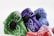 A collection of cloth masks featuring vibrant paisley patterns in different colors, including green, purple, blue, and red. Each mask has a black valve and a metal nose clip for a better fit. The patterns and bright colors create an eye-catching display.