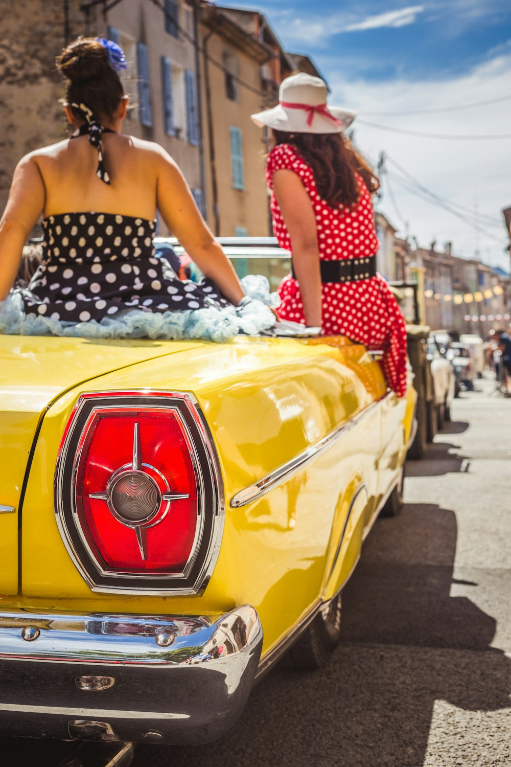 woman in black and white polka dot dress sitting on yellow car hood during daytime