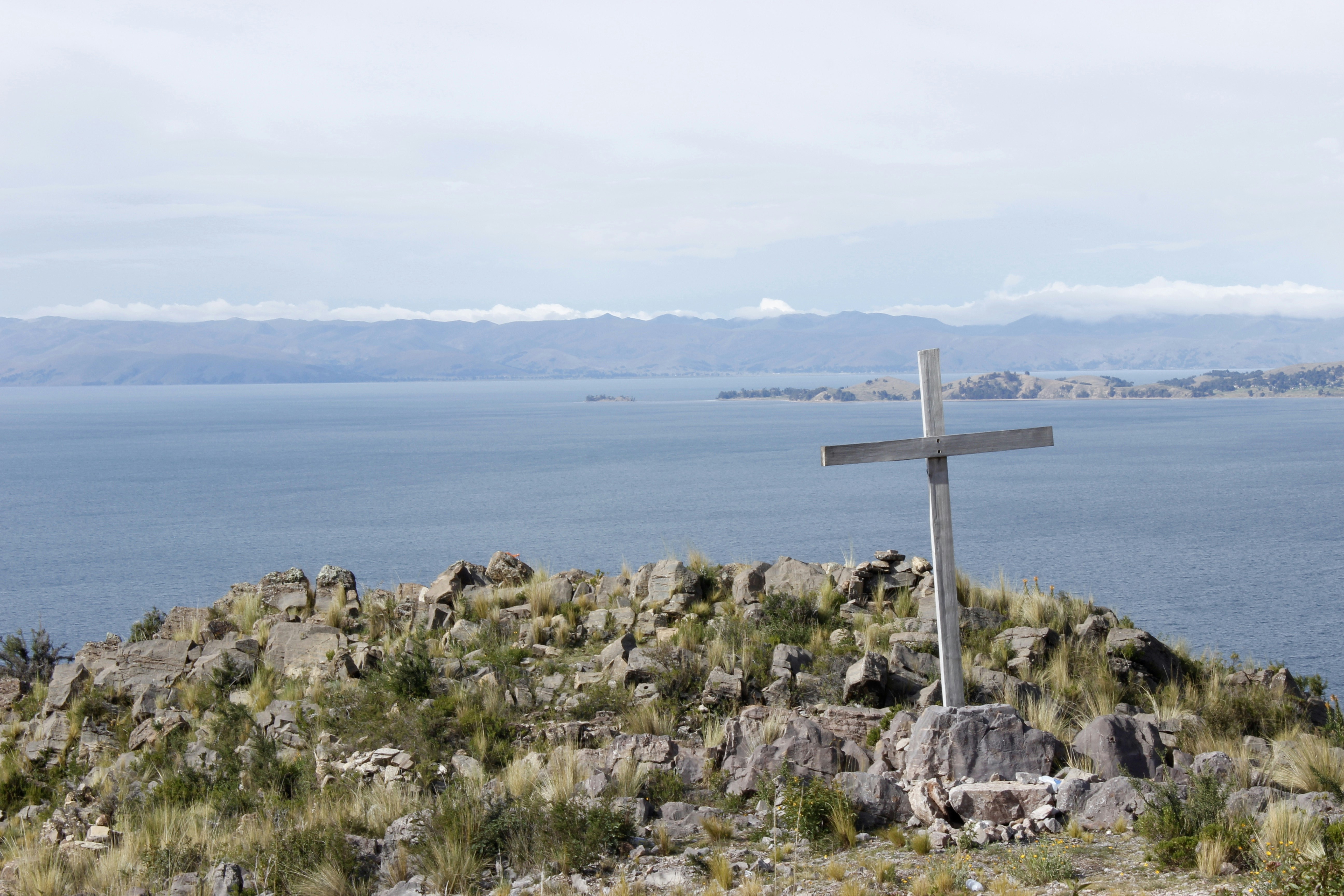 white cross on gray rock near body of water during daytime