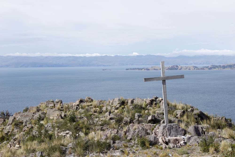 white cross on gray rock near body of water during daytime