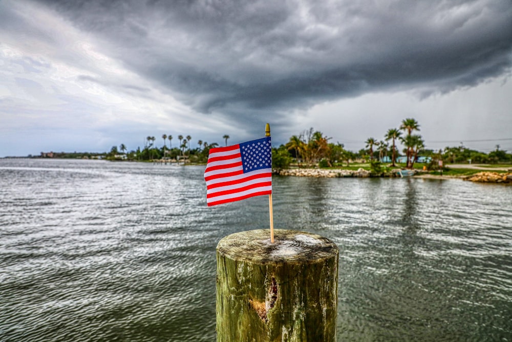 日中、水域の近くにある茶色の木製の支柱に旗を立てる米国