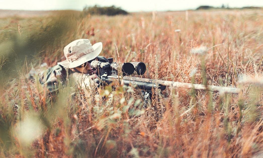 Hunter with scoped rifle aiming in an open field