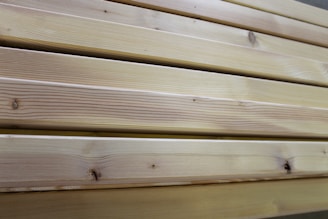 Close-up view of several neatly stacked wooden planks exhibiting natural grain patterns and a light tan color, indicative of unfinished or lightly finished wood.