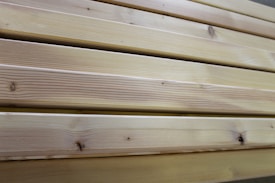 Close-up view of several neatly stacked wooden planks exhibiting natural grain patterns and a light tan color, indicative of unfinished or lightly finished wood.