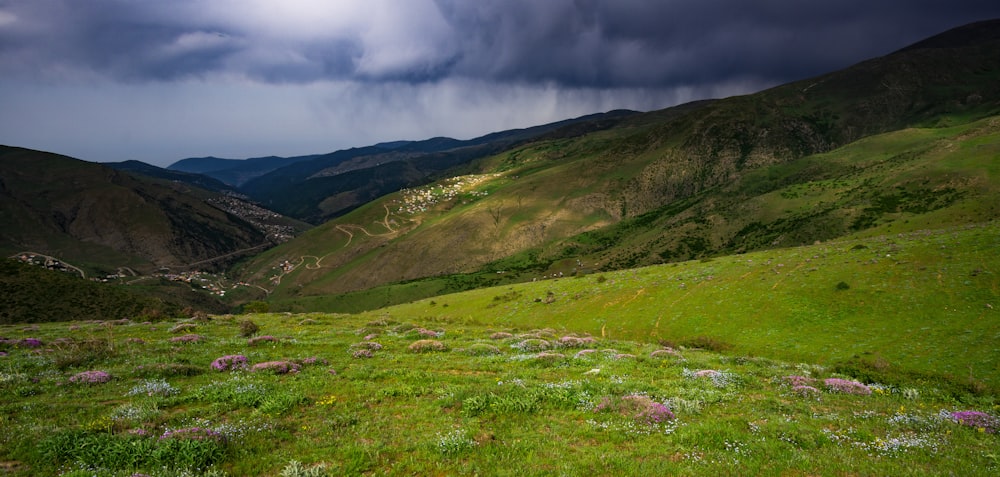 green grass field and mountains under white clouds and blue sky during daytime