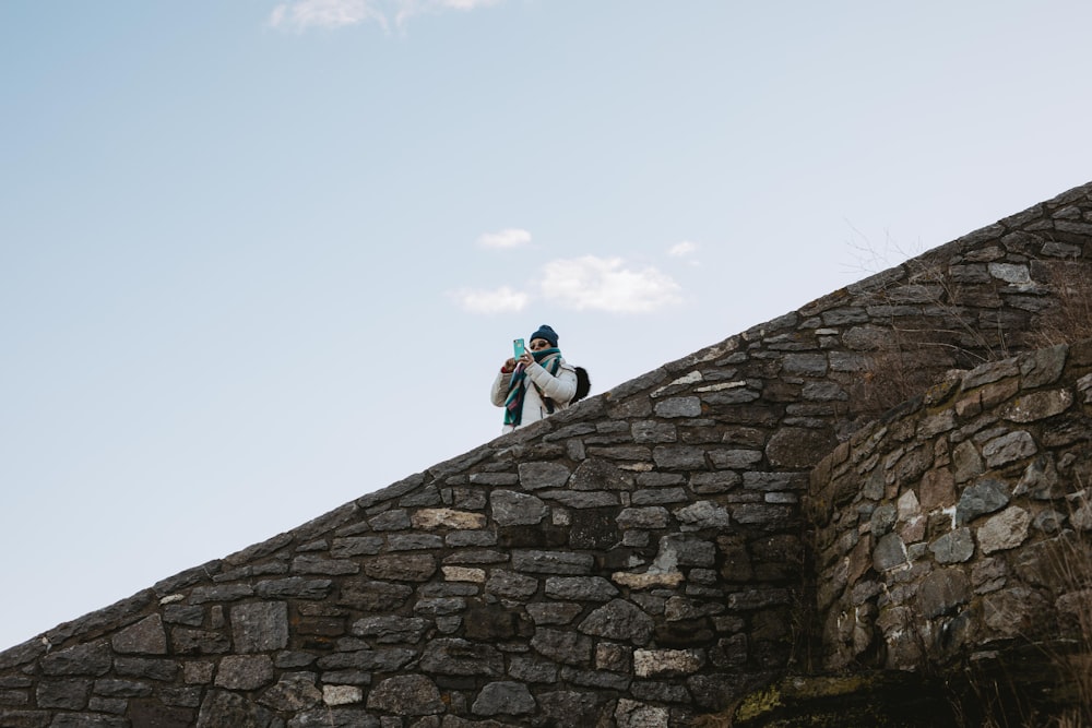 man in blue jacket and black pants climbing on gray brick wall during daytime