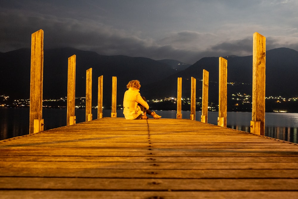 woman in white jacket and blue denim jeans standing on wooden dock during daytime