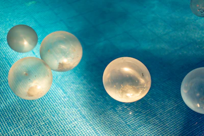 Close-up of floating photocatalyst spheres gently resting on a clear water surface under sunlight.