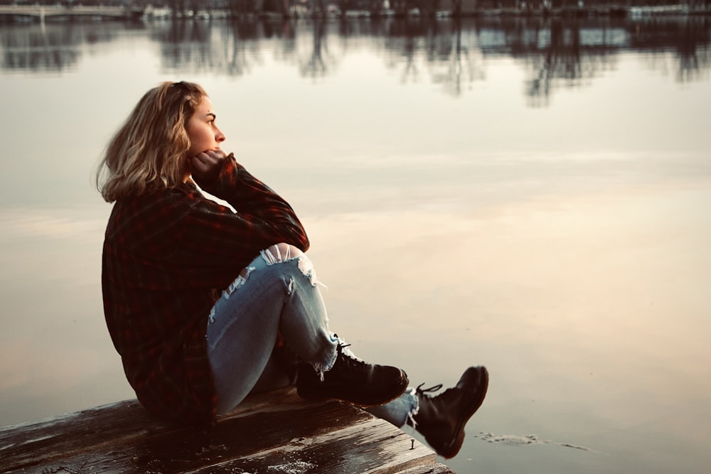 woman in black and red plaid long sleeve shirt and white pants sitting on brown wooden