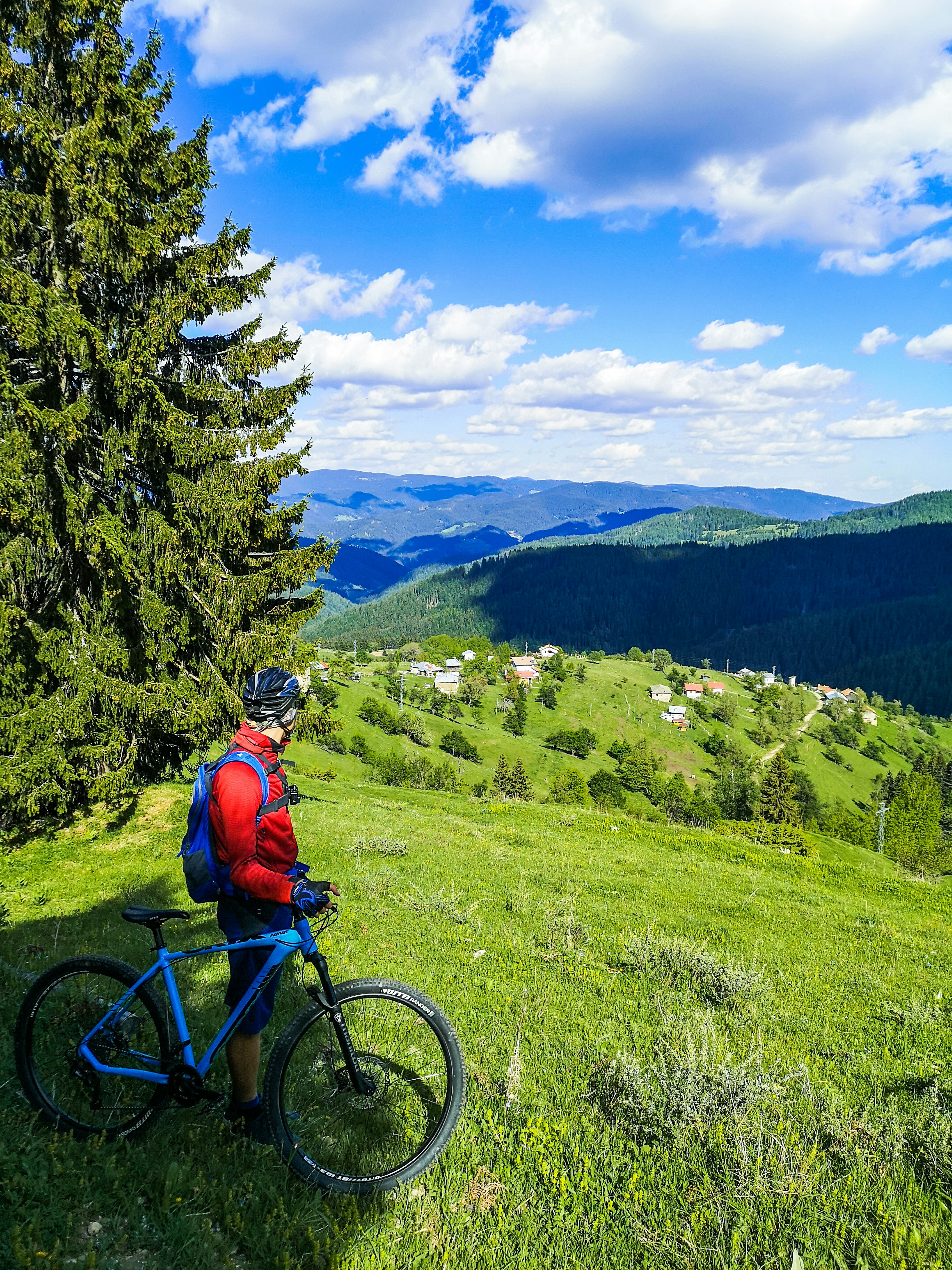 man in orange jacket riding blue mountain bike on green grass field during daytime