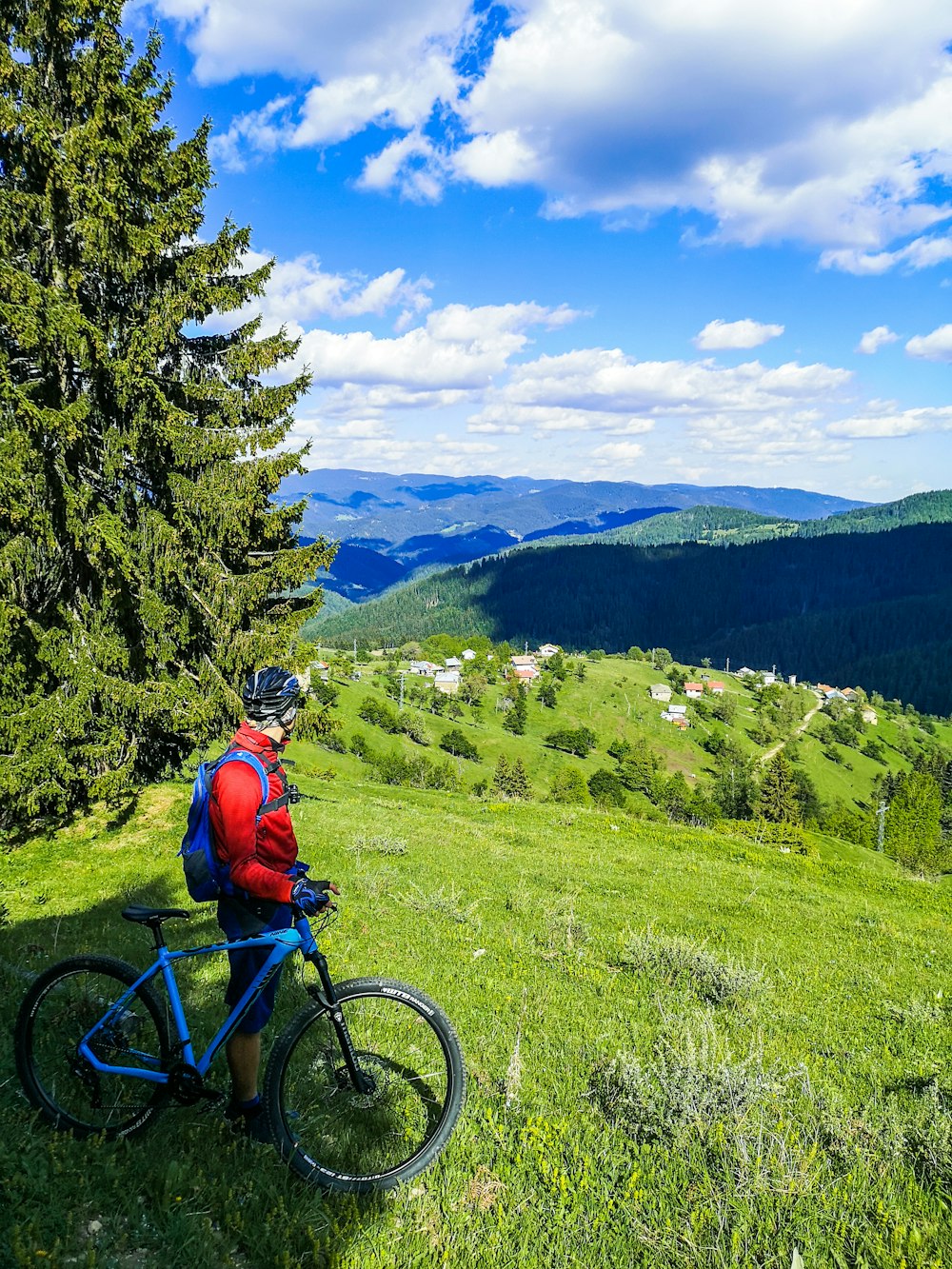 hombre con chaqueta naranja montando bicicleta de montaña azul en campo de hierba verde durante el día