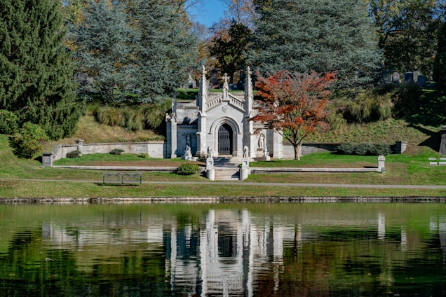 A serene funeral home entrance with white walls and dark orange accents, surrounded by gentle greenery.