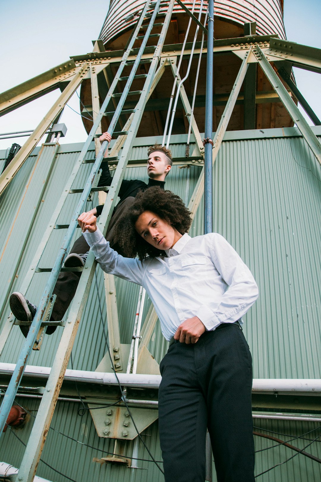 man in white dress shirt and black pants sitting on white metal ladder during daytime