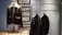 A display features three leather jackets. One is on a mannequin with a shearling collar, while two are hanging on a metal rack. The background includes a decorative panel with street names in bold capital letters.