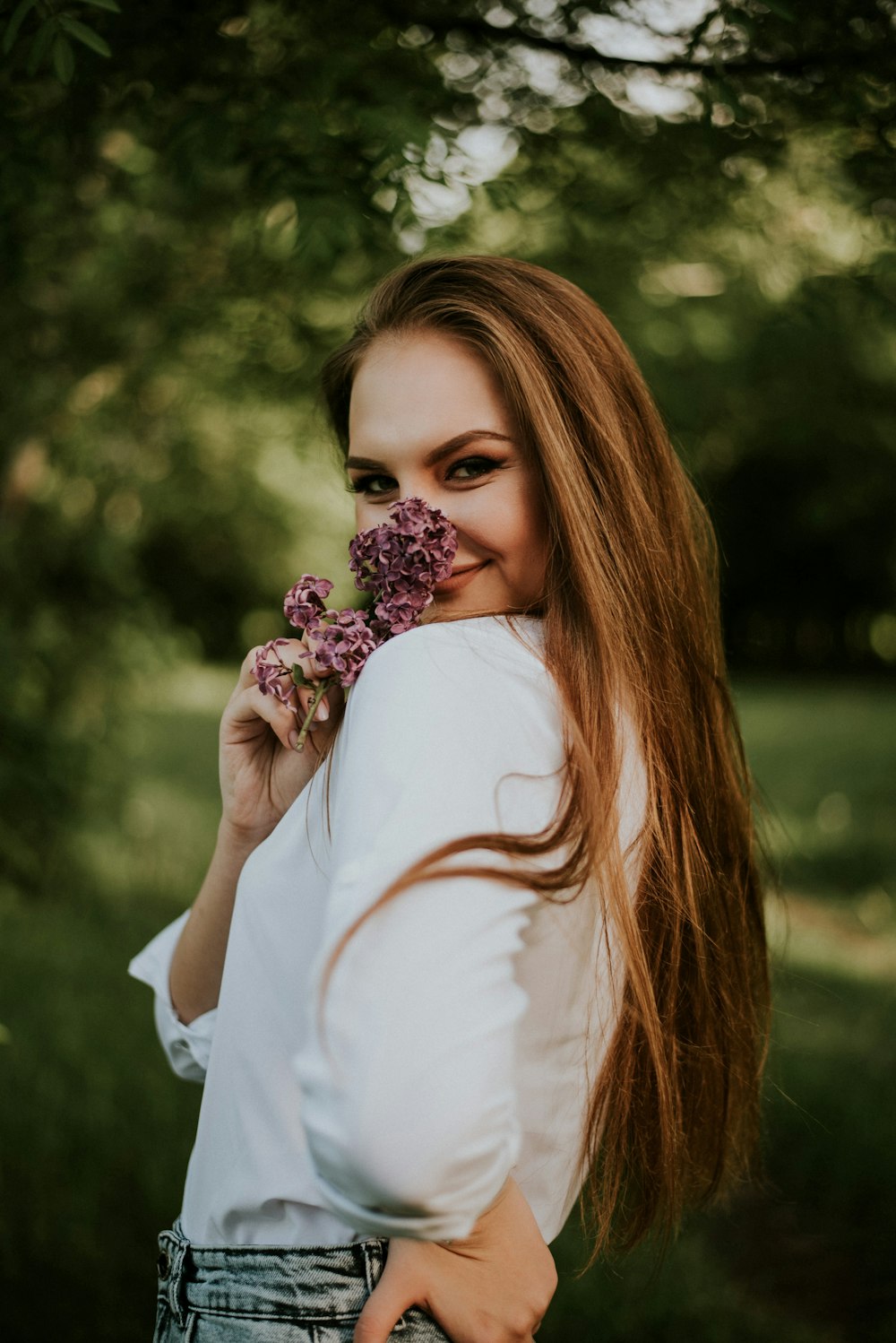woman in white long sleeve shirt holding pink flowers