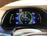 A car dashboard display showing various metrics including battery level, fuel range, odometer reading, and Bluetooth audio connectivity. The display includes indicators for power usage in kilowatts, EV range in miles, and a speedometer set to zero mph. The dashboard has a sleek, modern design with vibrant colors.