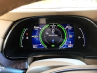 A car dashboard display showing various metrics including battery level, fuel range, odometer reading, and Bluetooth audio connectivity. The display includes indicators for power usage in kilowatts, EV range in miles, and a speedometer set to zero mph. The dashboard has a sleek, modern design with vibrant colors.