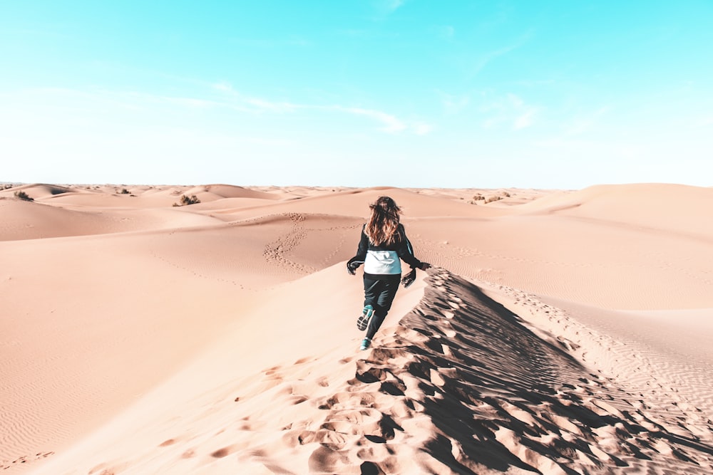 woman in black tank top and black pants walking on brown sand during daytime