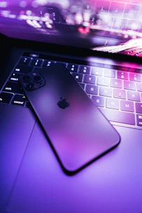 A sleek smartphone with a glowing blue screen resting on a modern black and white desk setup.