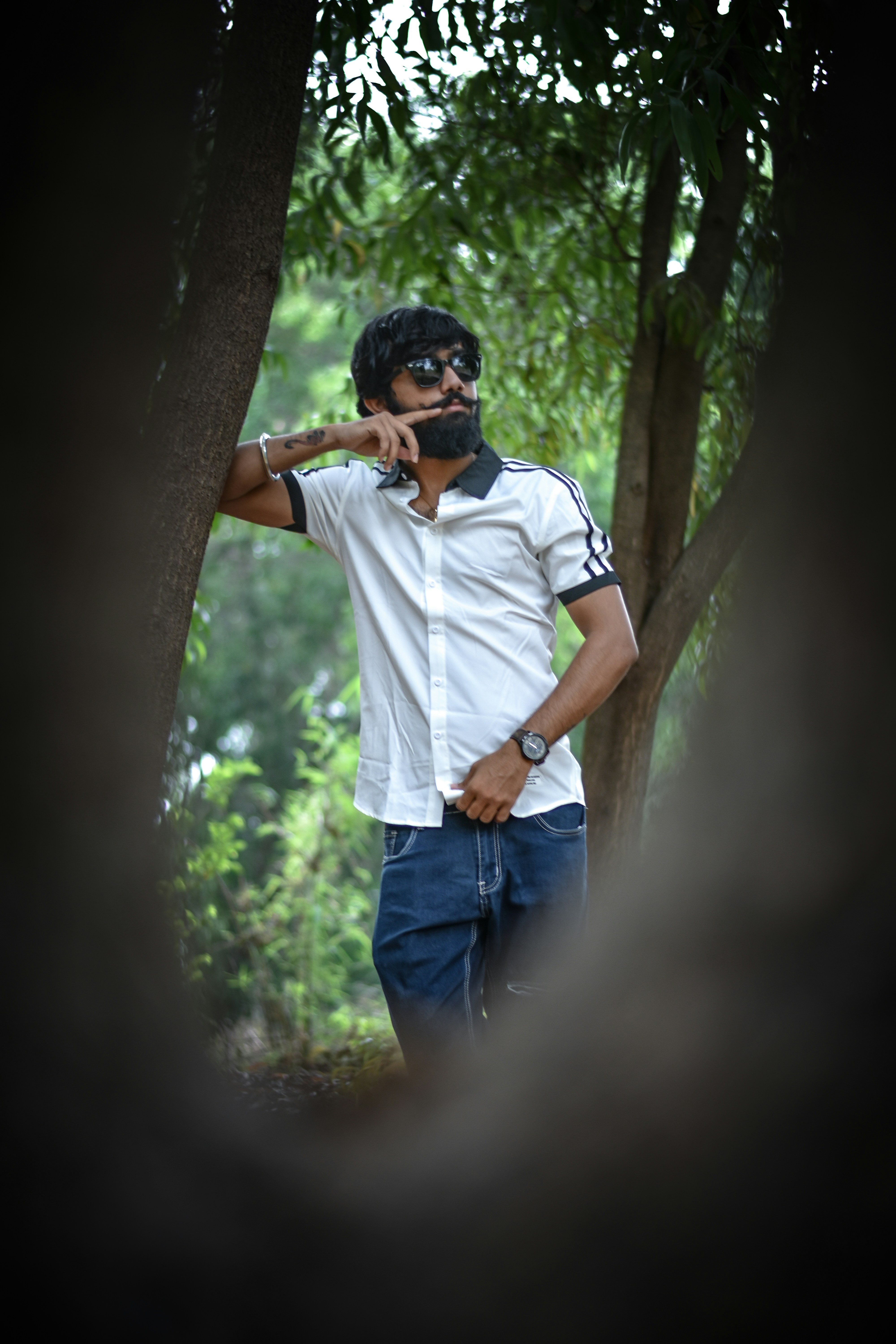 man in white crew neck t-shirt and blue denim jeans standing beside tree during daytime