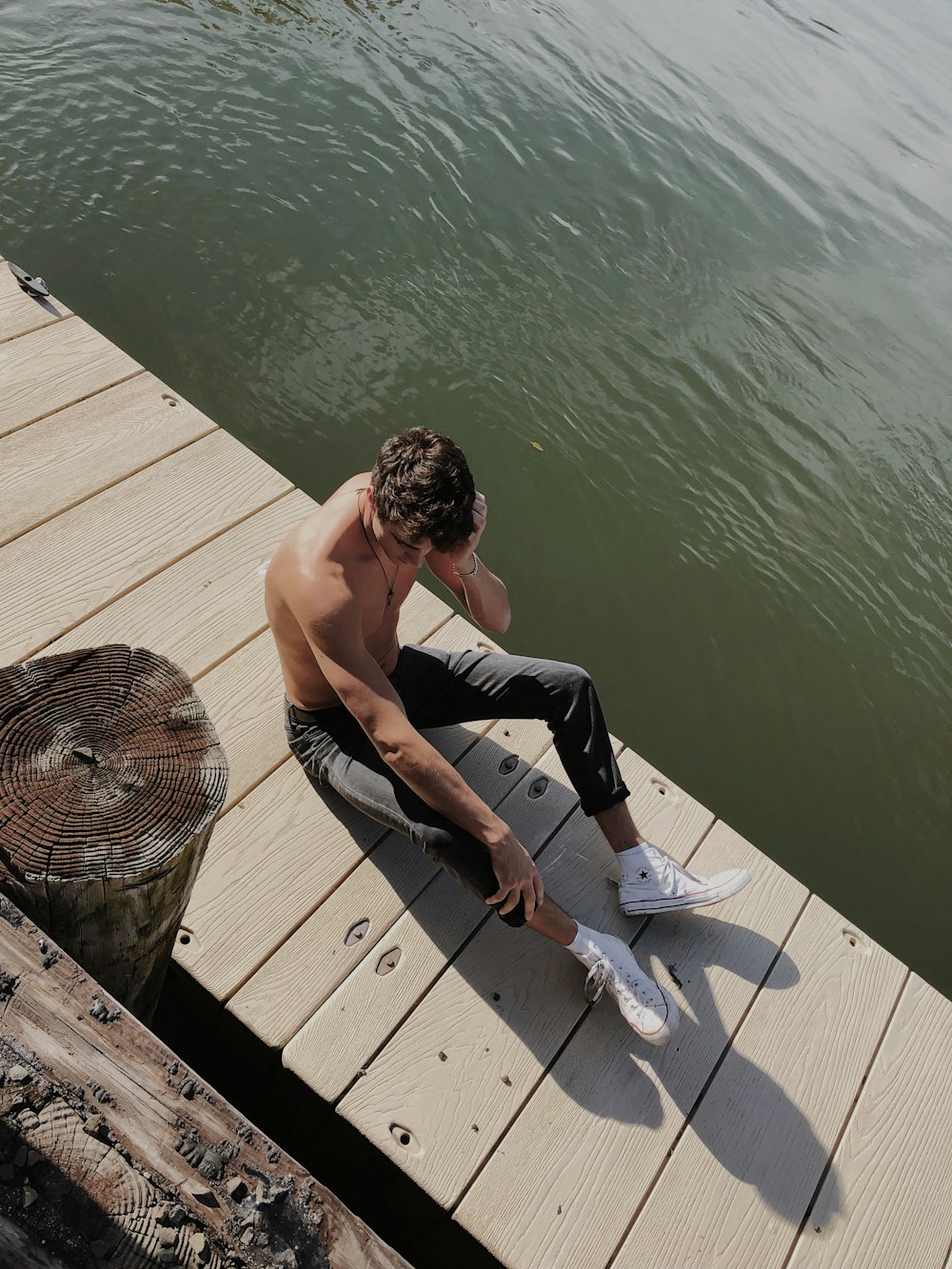 homme en pantalon noir assis sur le quai en bois brun pendant la journée
