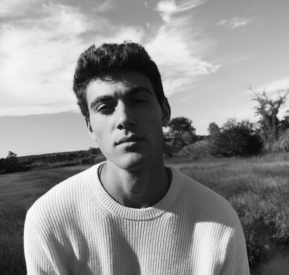 man in white crew neck shirt standing on grass field in grayscale photography