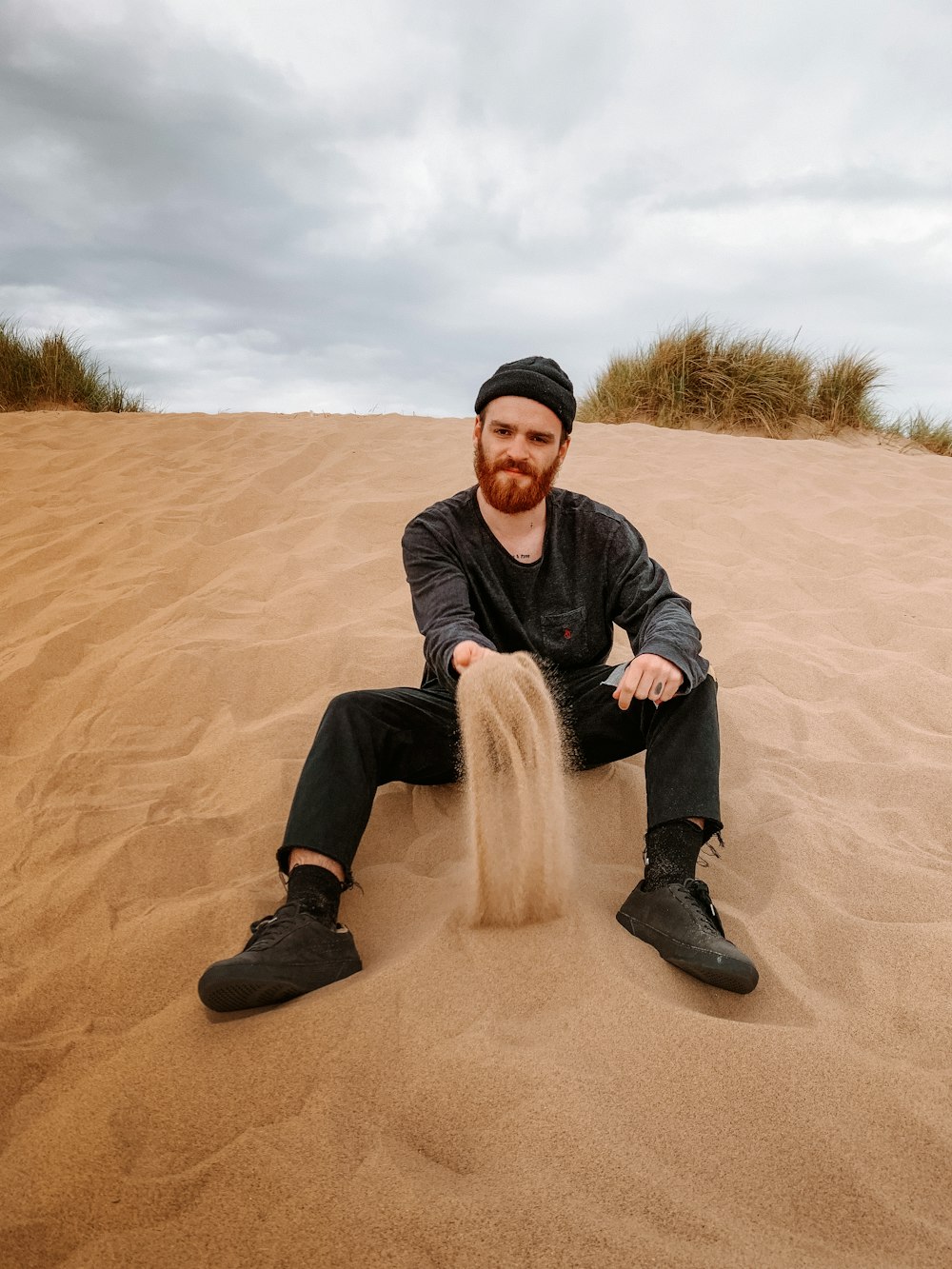 man in black jacket sitting on brown sand during daytime