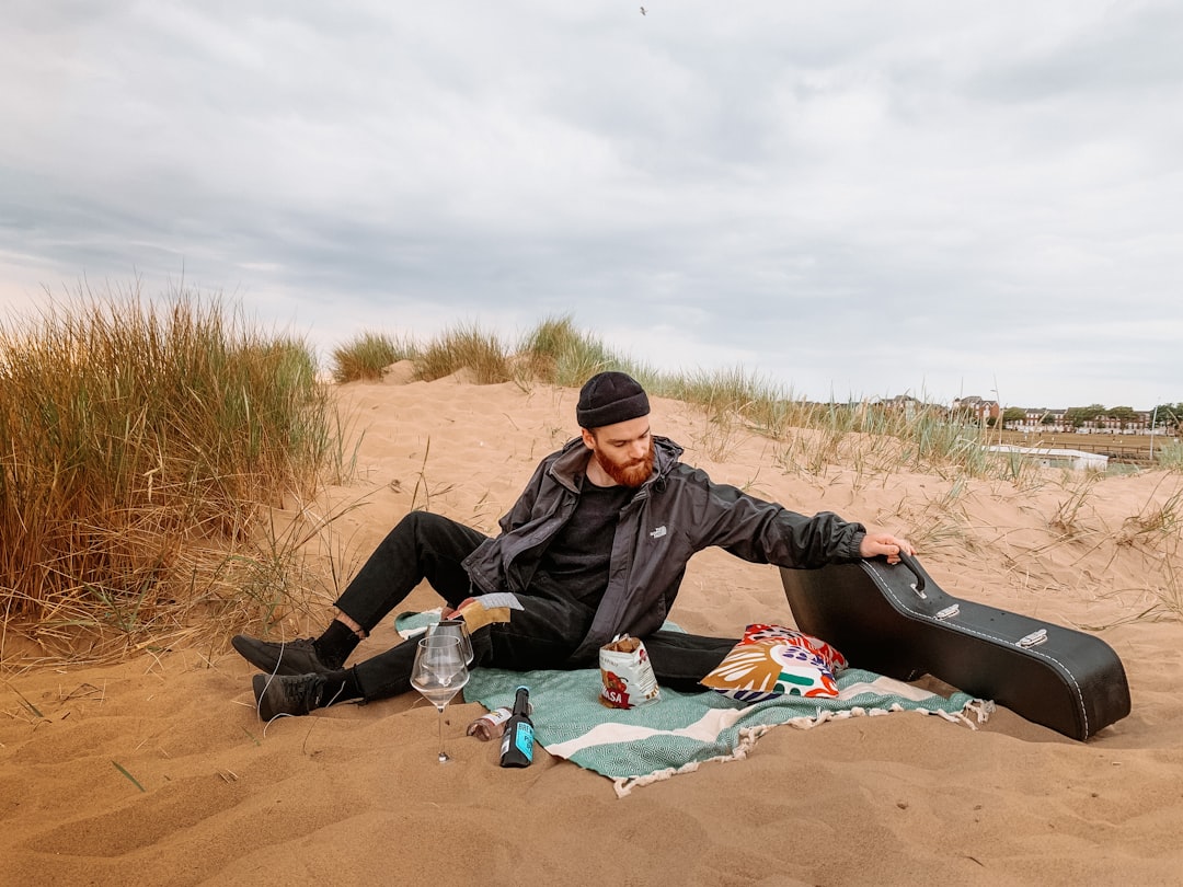 man in black jacket and black pants sitting on brown sand during daytime